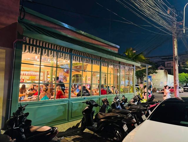 Bontà in the evening: tall green-framed windows under striped awnings and a busy dining room inside
