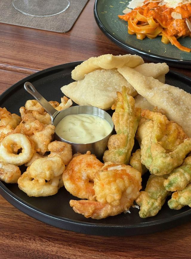 Fried calamari, prawns and vegetables on a black plate with a creamy dip