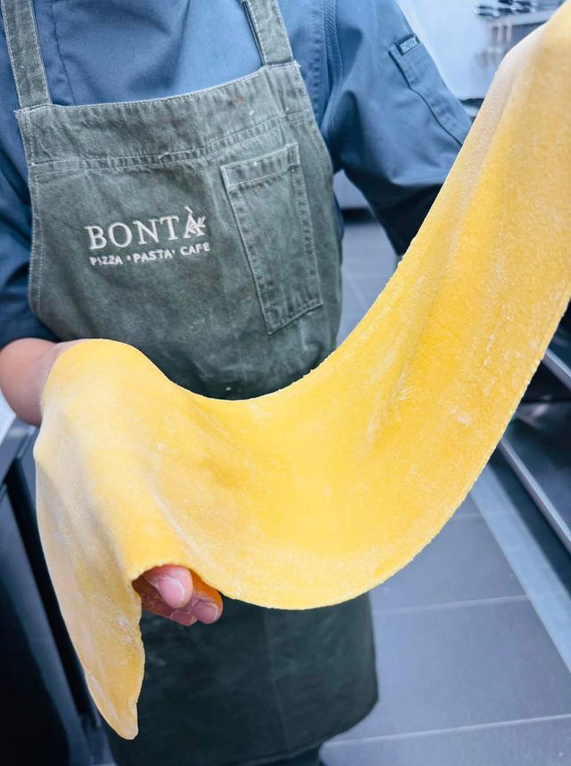 A chef in a Bontà apron holding up a long sheet of fresh egg pasta