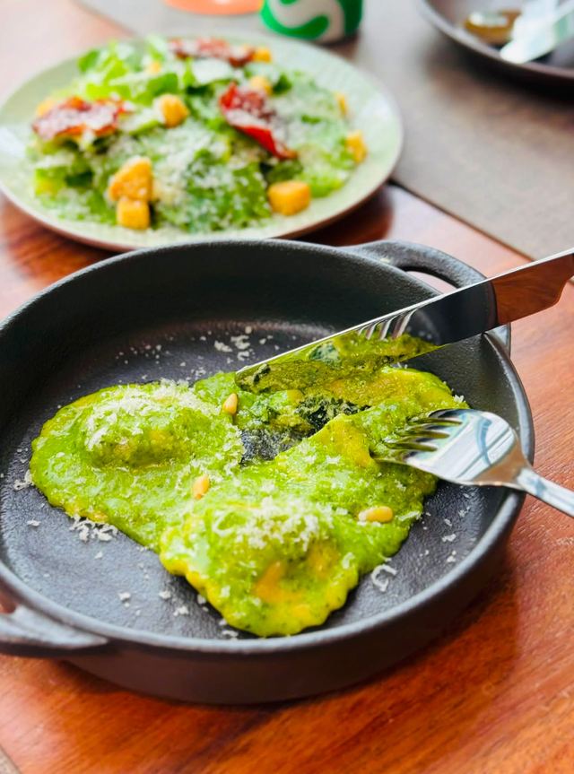 Ravioli in green pesto with pine nuts and parmesan, cut open to show the spinach filling